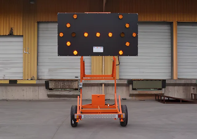 Carro flecha LED con el panel de flecha ámbar encendido, sobre su estructura naranja de transporte.