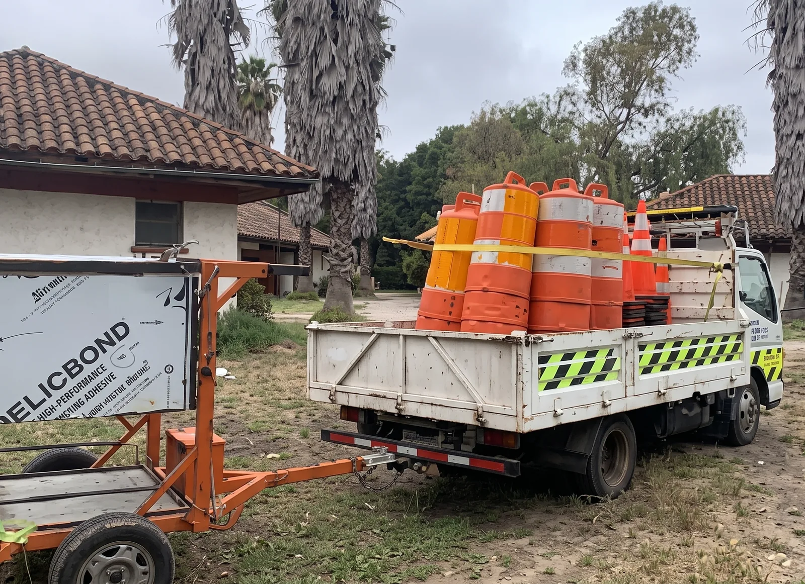Carro de señalización remolcado por un camión cargado con tambores de seguridad naranjos.
