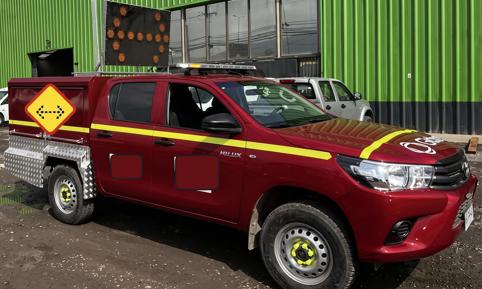 Camioneta Toyota Hilux roja de costado, con el panel flecha LED TEC-1130 levantado y caja de herramientas de aluminio.
