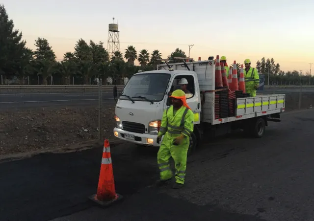Operario cargando conos de seguridad a un camión al atardecer, durante el retiro de una faena vial.